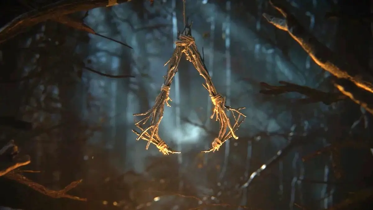 A triangular symbol made of woven twigs and branches hanging in a dark, foggy forest