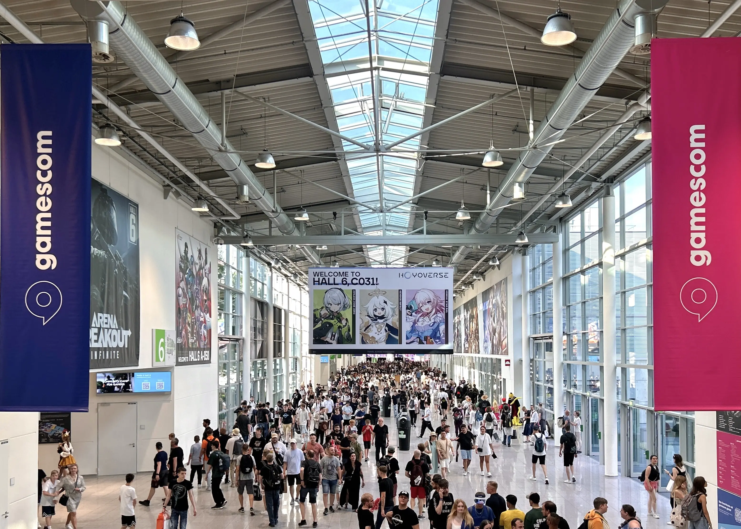 Busy Gamescom exhibition hall with banners and crowds of visitors.