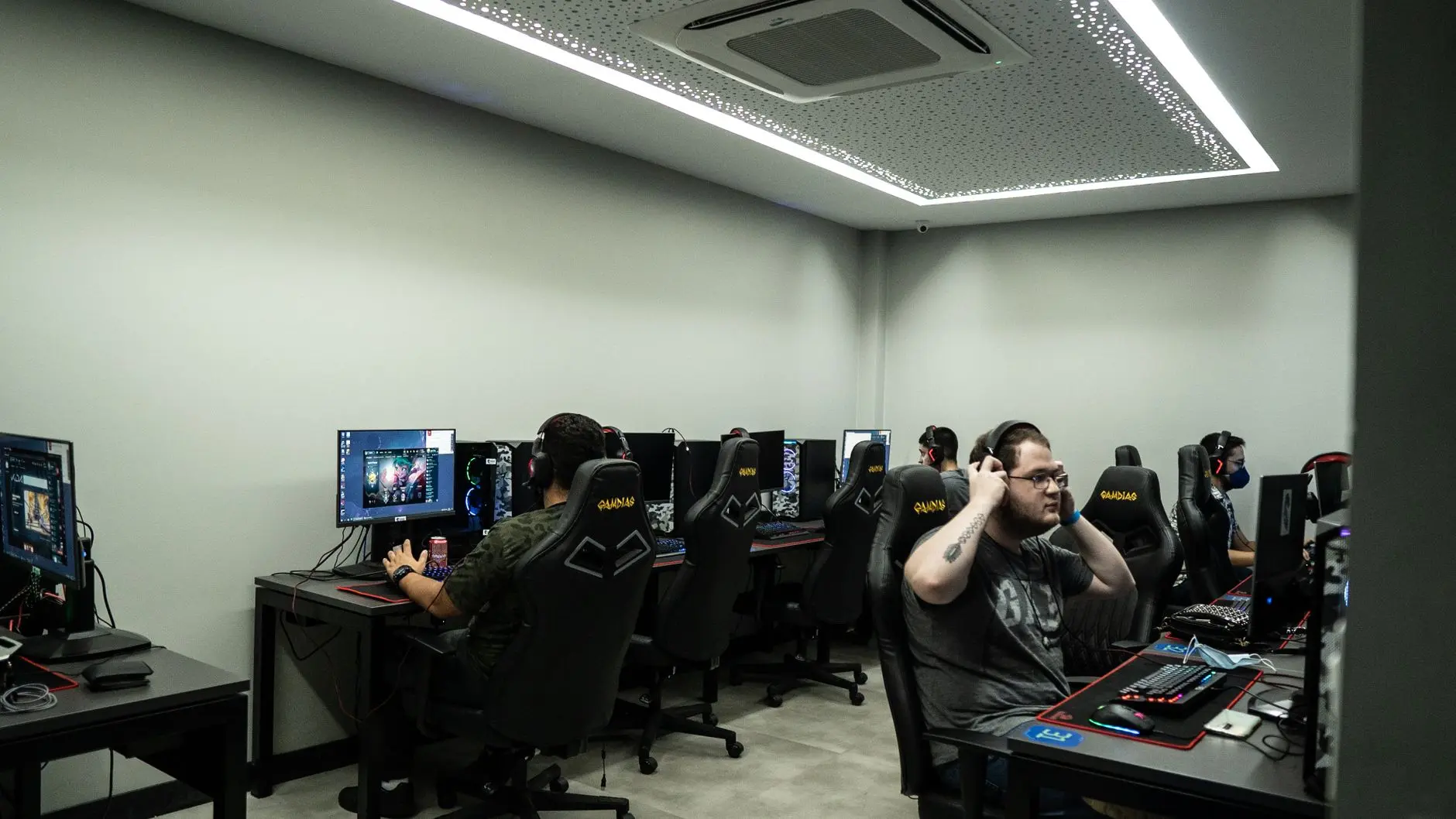 Professional gamers wearing headsets sitting at a row of gaming PCs in a dedicated esports training room